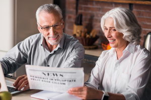 Two older people reading a newspaper together in front of them