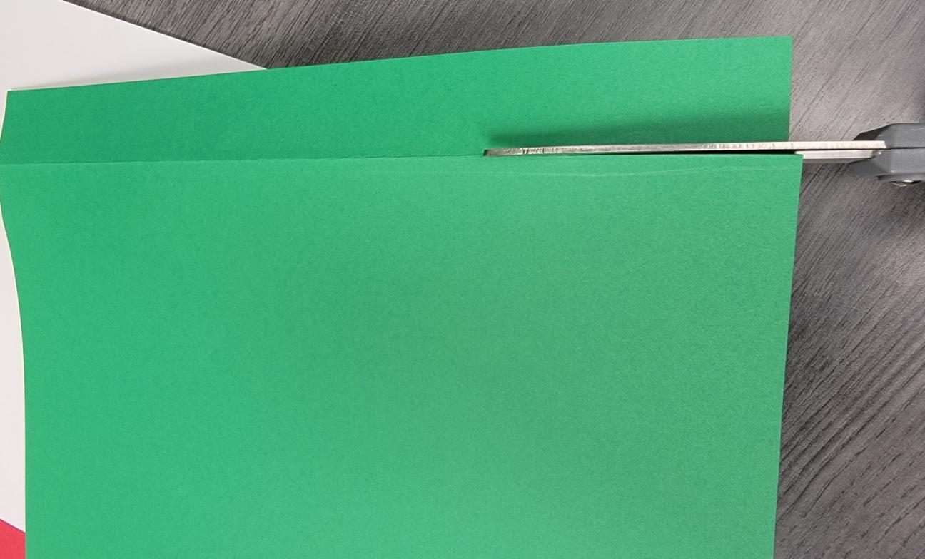 Using scissors to cut a narrow strip from the edge of the green paper.