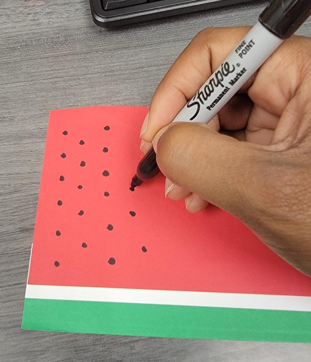 Drawing seeds on the red area of the paper, using a black marker.