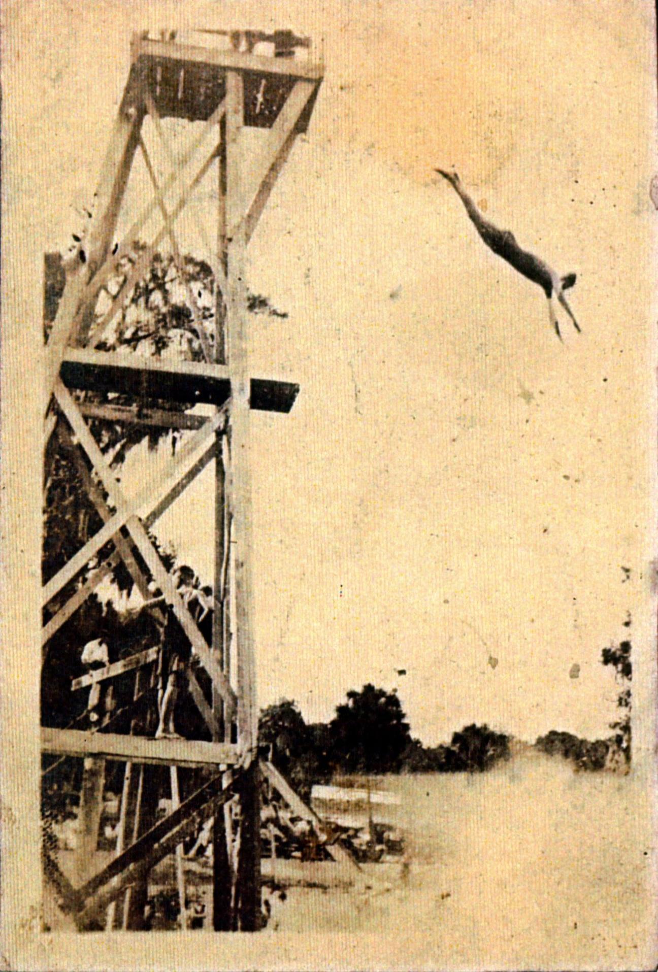 person mid-air diving from high platform into lake