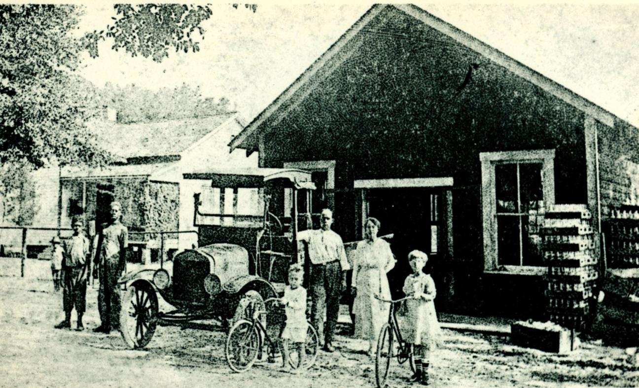 people standing in front of an old car and the Coca Cola plant in Hawthorne