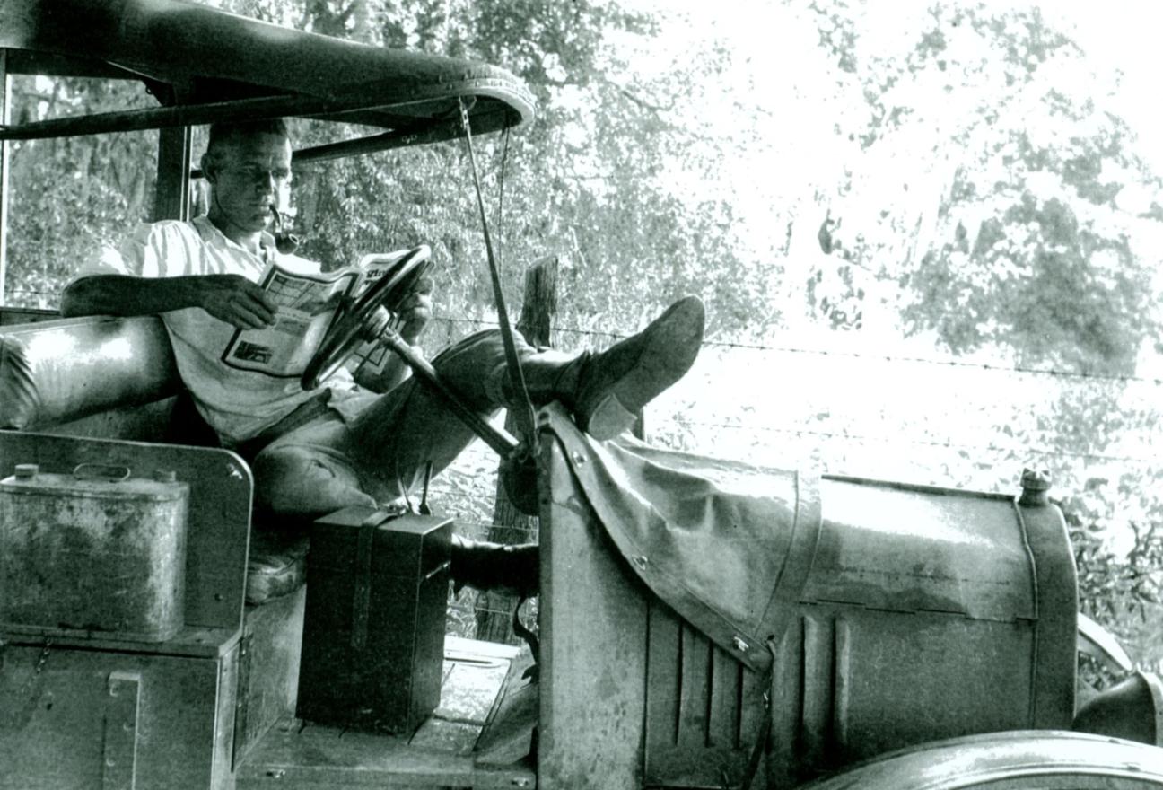 man in car reading a newspaper and smoking a pipe