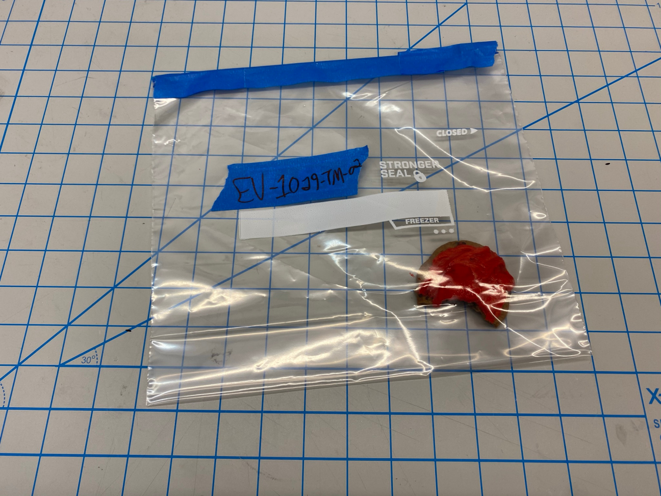 Photo of an evidence bag, which contains a cookie with red frosting that was found on top of the victim's body. A bite has been taken.