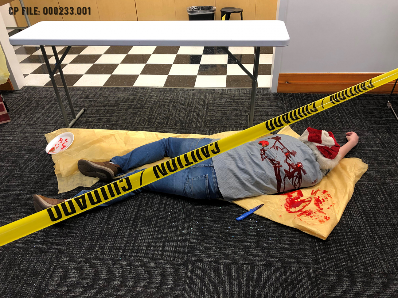 image of a dead stabbed body lying on a tablecloth. The image is cut through with police tape.