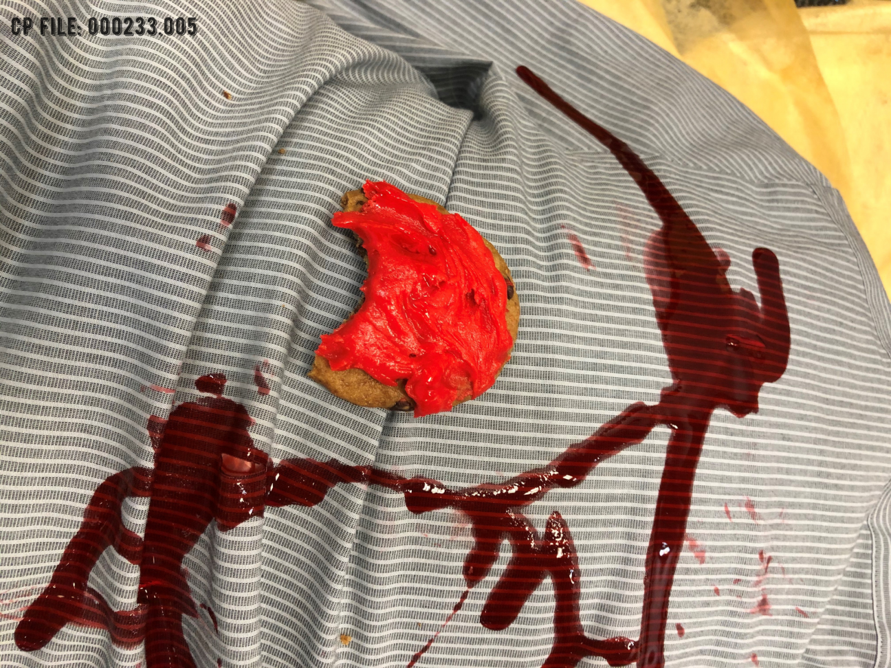 A close up of a cookie with red icing with one bite taken out of it. The cookie is resting on top of a stabbed body