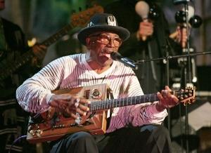 an older african american man sitting down playing a guitar