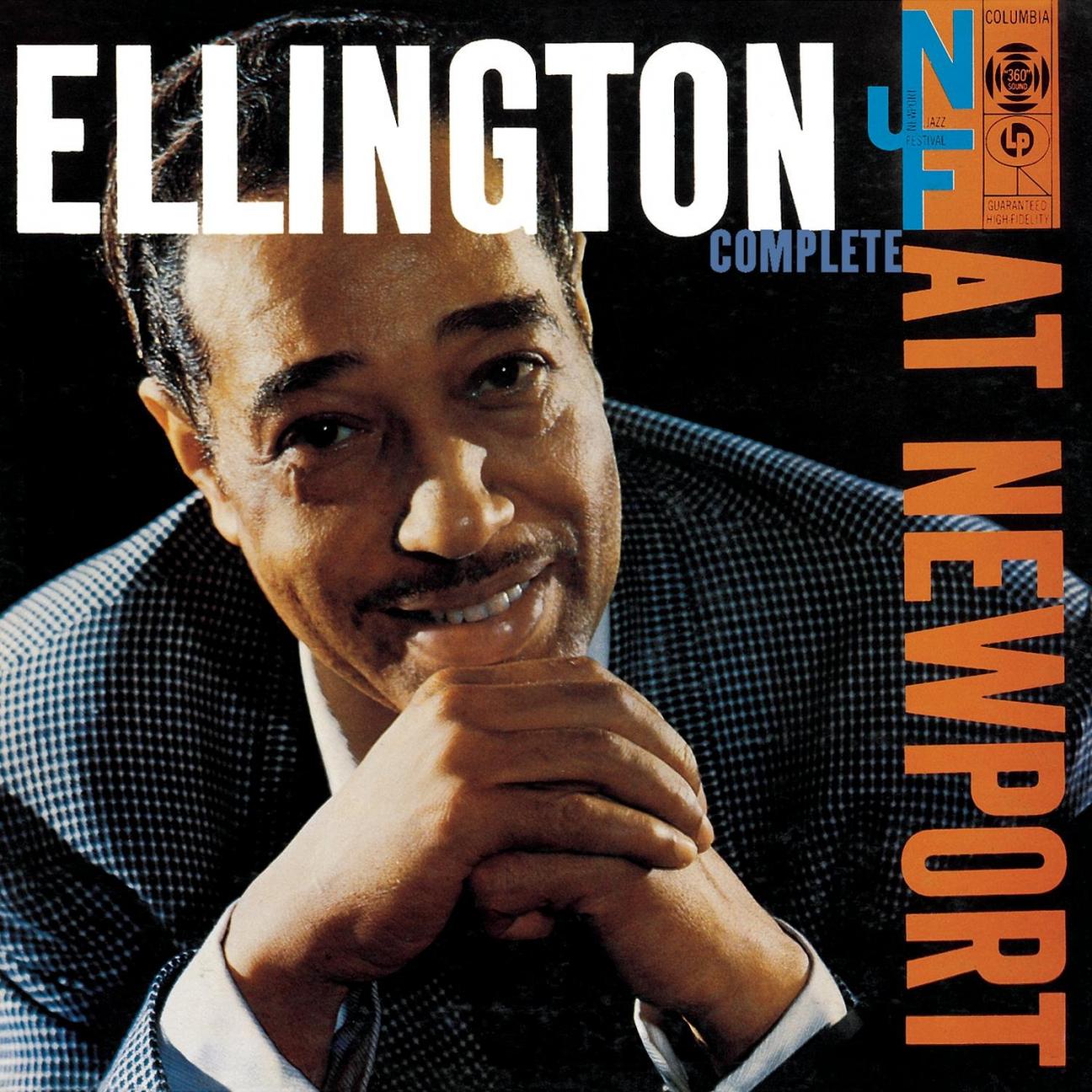 The cover of "Ellington at Newport 1956" album which has the title in white and orange across the top and down the side, and has a color photo of Duke Ellington smiling with his chin on his clasped hands.