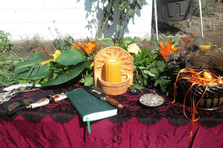 A Litha altar featuring herbs, ceremonial tools, a candle, and sun icons.