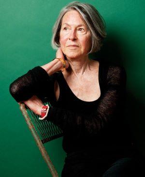 A picture of poet, Louise Gluck, wearing a black dress with a green background.