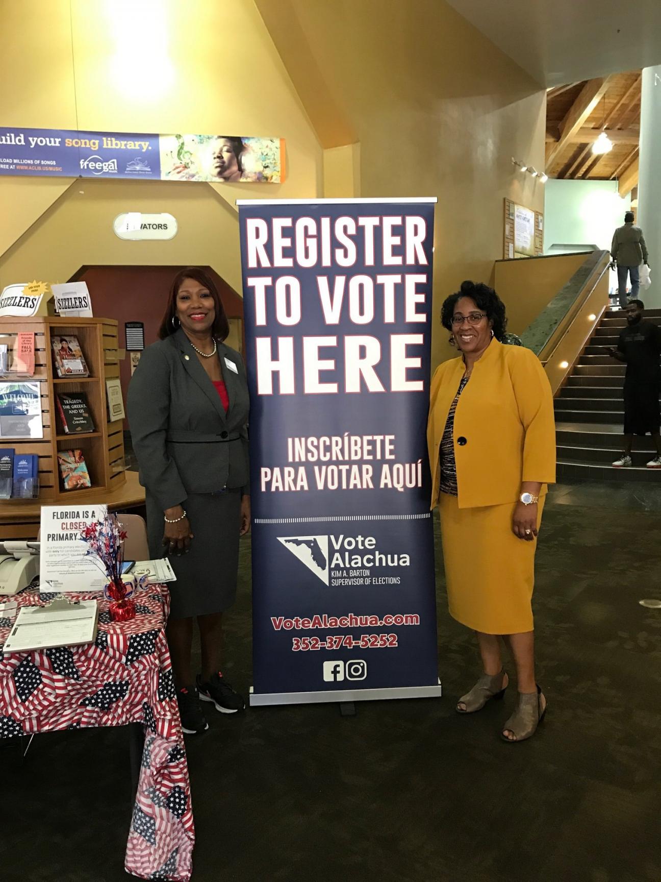 Shaney Livingston and Kim Barton standing next to a sign encouraging peopel to register to vote at the Headquarters Library