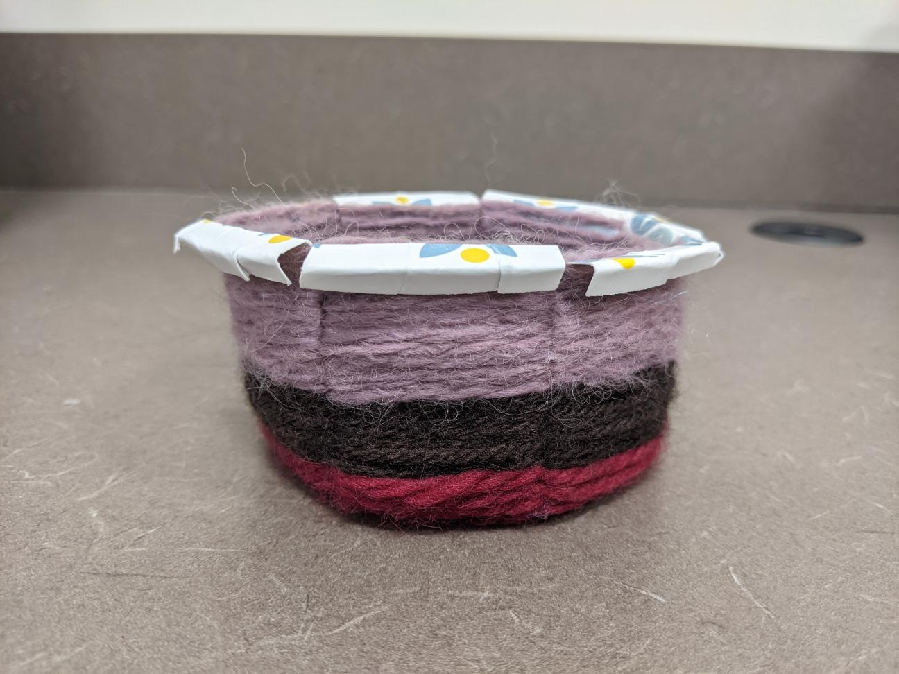 The finished yarn basket! It is small and has stripes of red, brown, and purple