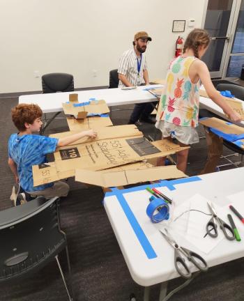 Two students build model bridges with cardboard and tape.